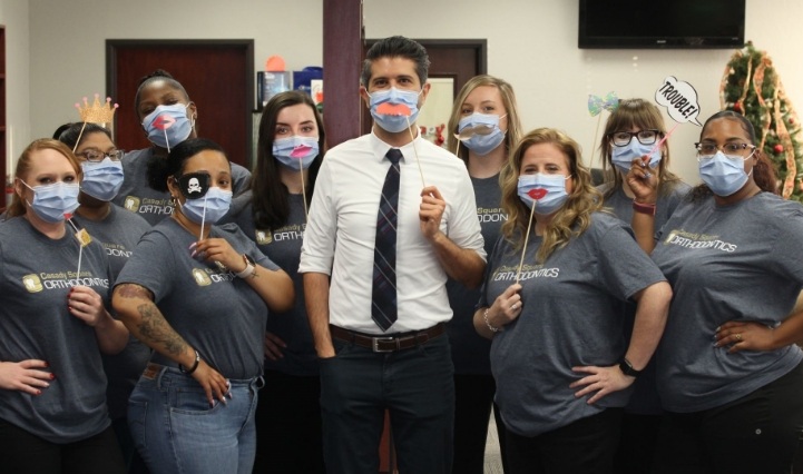 Oklahoma City orthodontist and team wearing face masks each holding a stick with a fake mustache or lips up to their faces