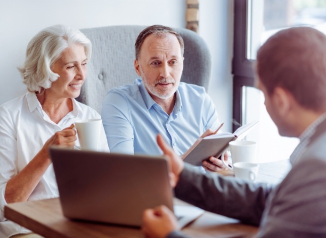 Man and woman sitting across desk from man showing them his laptop