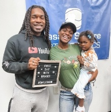 Mother and father with their child in orthodontic office holding sign saying first day with braces