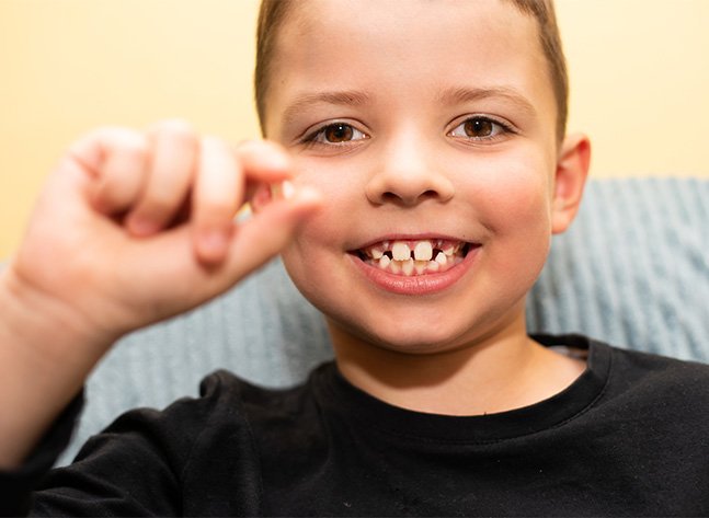 Smiling young boy holding his lost tooth