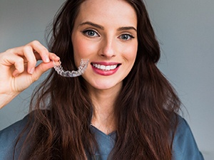 Young woman smiling while holding Invisalign aligner