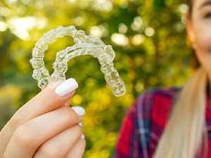 Smiling patient holding up Invisalign Teen aligners