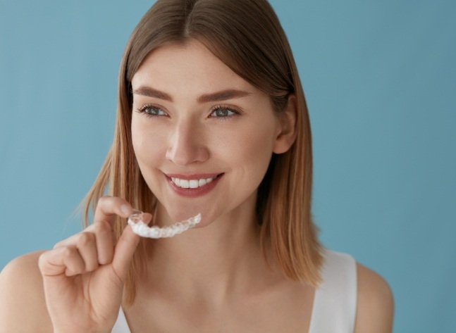 Woman holding Invisalign clear aligner against turquoise background