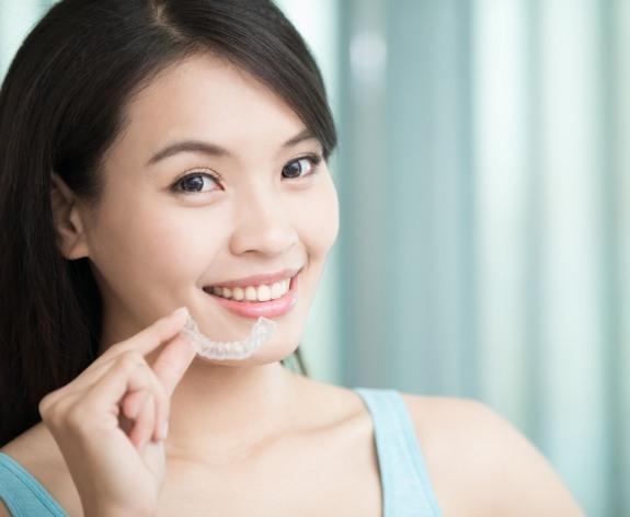 Woman holding Invisalign aligner next to her smile