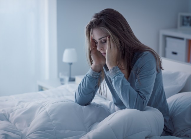 Woman sitting up in bed rubbing her temples in frustration