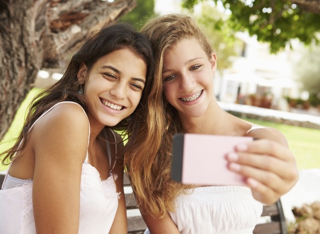Two teenage girls taking selfie on park bench