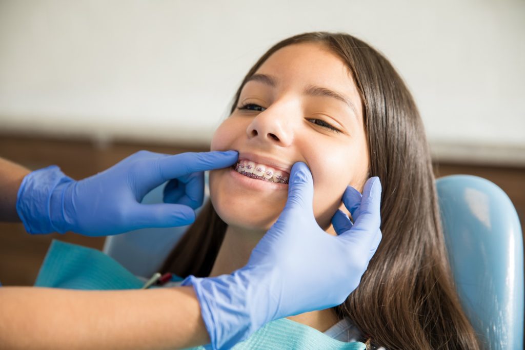 Orthodontist with blue gloves examining patient's braces