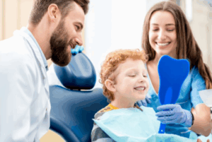 Child smiling while orthodontist and assistant show him his teeth with a small mirror
