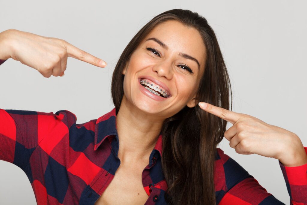 Woman in red and black checkered shirt pointing to her smile with braces